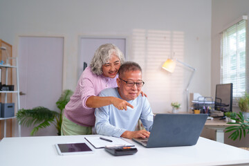 Senior Asian Couple Enjoying Retirement at Home Together Using Laptop for Online Shopping Healthcare Insurance and Stay Connected with Family and Friends
