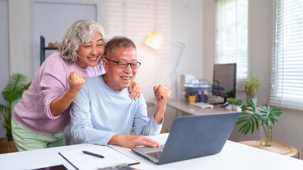 Happy Asian Older Couple Celebrating Success with Laptop in Home Office. Retirement Lifestyle,...