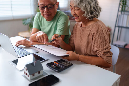 Senior Asian Couple Planning Finances at Home with Laptop, Calculator and Documents. Retirement Planning, Home Investment and Estate Planning for Older Adults - Powered by Adobe