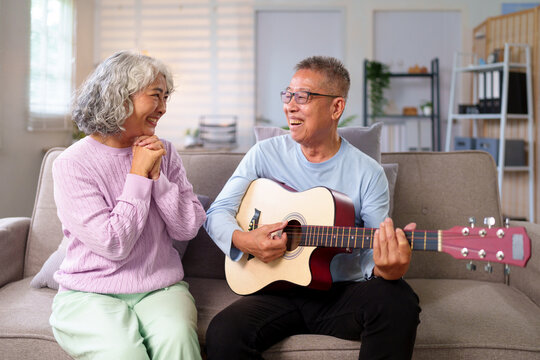 Senior Asian Couple Enjoying Music at Home Asian Man Playing Guitar for his Beautiful Asian Wife Retirement Living and Quality Time Together