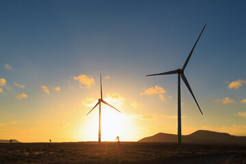 Wind turbines silhouette during a breathtaking sunset behind mountains, highlighting renewable...