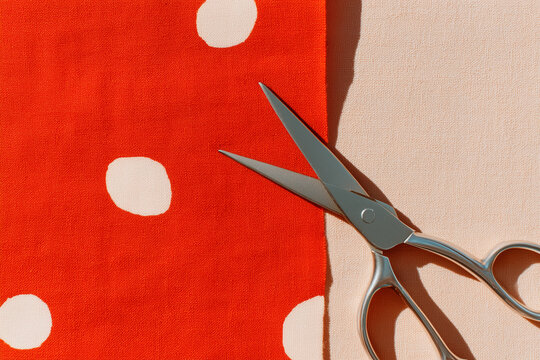 Scissors placed on vibrant red polka dot fabric next to neutral fabric. Bright workspace highlights textile design and sewing creativity. Concept of crafting, fashion design, handmade projects - Powered by Adobe