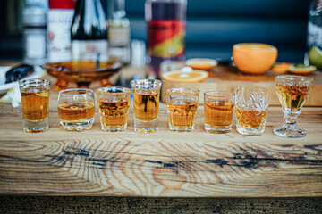A lineup of whiskey glasses on a wooden table showcases a diverse selection of amber spirits, set...