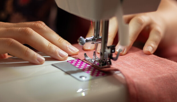 A woman sews on a sewing machine. Hands of a craftswoman. Overlock on fabric. Textile business, tailoring. Hobbies and crafts. Close up photo