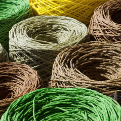 Natural raffia fibers are wound into spools. Skeins are beige, brown, green and yellow. The texture...