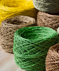 Natural raffia fibers are wound into spools. Skeins are beige, brown, green and yellow.