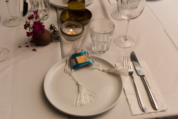 Table setting, white plate and glassware and treat bag on a white table cloth at a banquet dinner.