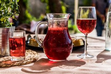 A clear glass pitcher and glasses of freshly brewed, deep burgundy, cold Hibiscus herbal tea