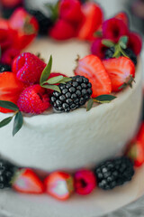 A beautifully decorated white cake adorned with fresh strawberries, raspberries, and blackberries, creating a vibrant and appetizing centerpiece for any celebration