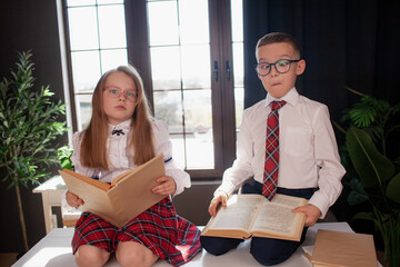 A 7-year-old child in glasses dressed in  school uniform poses at the school table indoor
