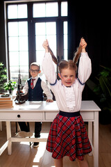 A 7-year-old child in glasses dressed in  school uniform poses at the school table indoor The boy and girl looks to the microscope