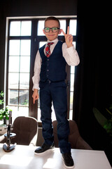 A 7-year-old child in glasses and dressed  school uniform poses at the school table indoor