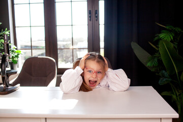 A 7-year-old child in glasses and dressed  school uniform poses at the school table indoor