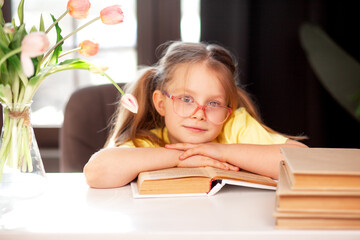 A 7-year-old child in glasses and  poses at the school table indoor