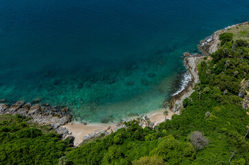 An stunning aerial view showcases a picturesque beach surrounded by lush green trees and ocean