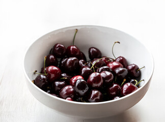 dark sweet cherries in a white ceramic bowl on a bright background