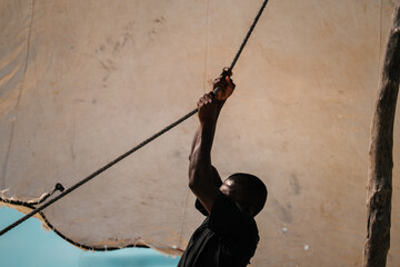 African sailing boat, sailor hoisting sails on a wooden boat