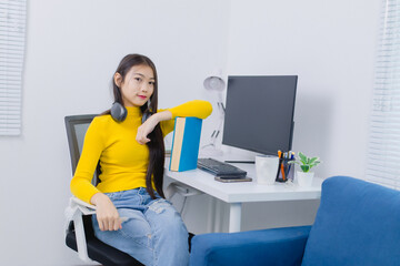 Young asian woman is working from her home office, sitting comfortably at her desk with headphones...