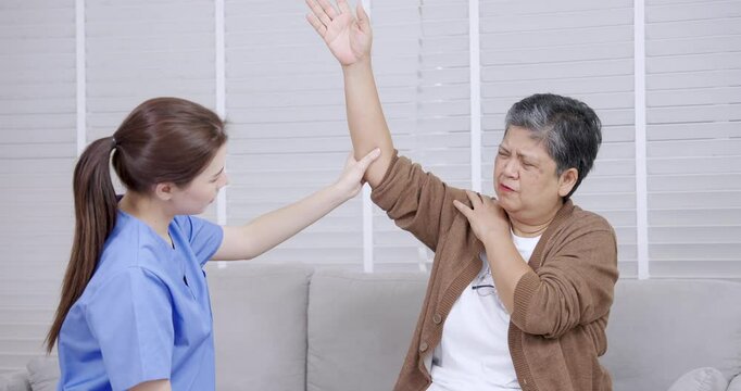 Asian senior female raising arm with support from Caucasian young female physiotherapist during upper limb rehabilitation exercise to improve joint mobility and reduce discomfort