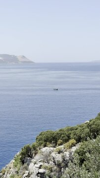 A boat sails on the sea against the backdrop of mountain hills and greenery (vertical)