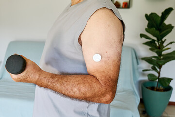 Unrecognizable mature man with diabetes and continuous glucose monitor on his arm making sport exercises at home