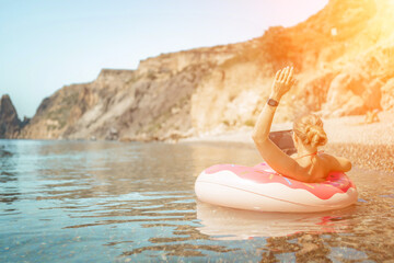 Woman laptop sea. Freelancer woman in sunglases floating on an inflatable big pink donut with a laptop in the sea. People summer vacation rest lifestyle concept