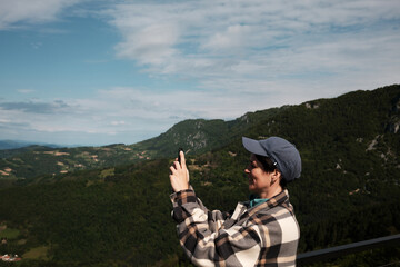 Woman takes a photo with her phone, capturing the mountain landscape from a high viewpoint in...