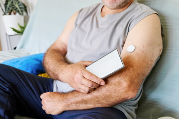 Unrecognizable mature man with diabetes and continuous glucose monitor on his arm using mobile app for checking his health
