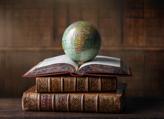 Old globe lying on an open book in a library. Conceptual background on history, education, literature topics. Translation of book titles - history of England, ancient history.