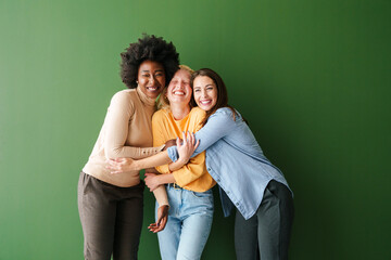 Three Multicultural Friends Hugging and Smiling in Casual Clothing Against a Bright Green Background