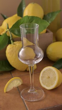 An elegant glass of Italian limoncello surrounded by fresh lemons, orange slices, and citrus leaves. Bright and refreshing still life with natural light and warm tones. High quality FullHD footage