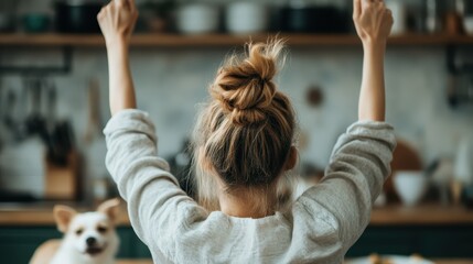 Fototapeta premium A young woman with a messy bun is raising her arms in celebration at home, surrounded by a vibrant kitchen atmosphere, accompanied by a cute dog, expressing joy and enthusiasm.