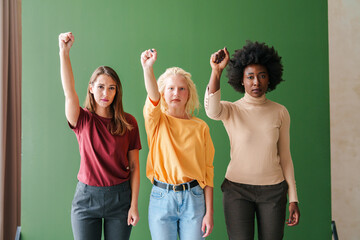Diverse Group of Women Expressing Strength and Unity with Raised Fists on a Minimal Green Backdrop