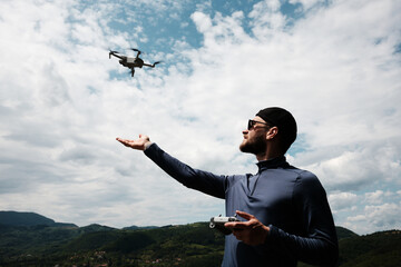 Man launches a drone with one hand while holding the remote in the other, standing on a high...