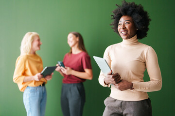 Confident Young Woman Engaged in Technology with Diverse Group of Young Adults Against a Green Indoor Background