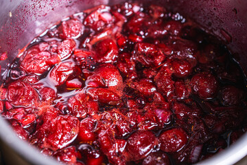 Cherry jam or sauce is cooked in a saucepan. Close-up. Background.