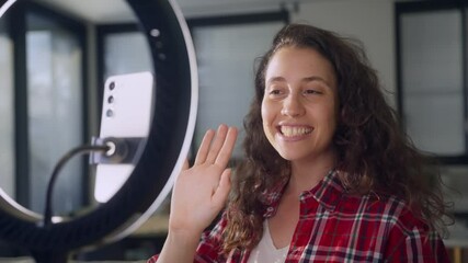 Woman pressing record button and greeting online fans and followers on vlog. Live streaming from her apartment young content creator or influencer is filming herself with mobile phone and ring light - Powered by Adobe