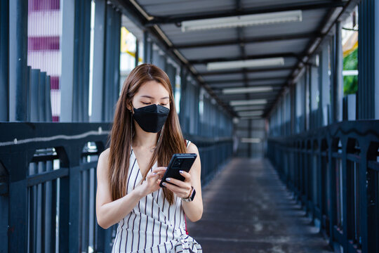 Asian woman using a smartphone while walking on an elevated walkway in the city