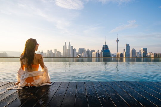 A woman in a bikini enjoys the rooftop pool and skyscrapers in a modern city