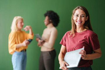 Smiling Young Woman Holding Tablet in Technology Setting with Diverse Group Discussion Behind Her