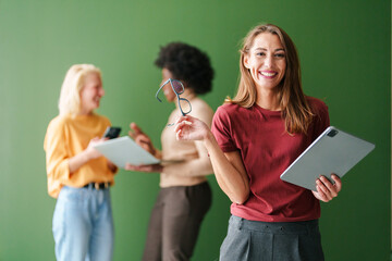 Diverse Group of Young Professionals with Tablets and Smartphones in Contemporary Office Space with Green Background