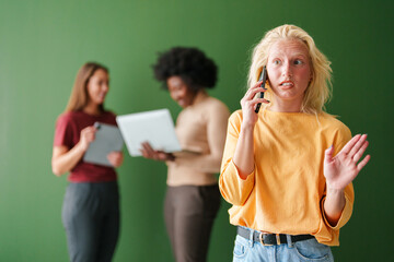 Young Blonde Woman on Phone with Diverse Group of Adults Using Technology in Minimalist Indoor...