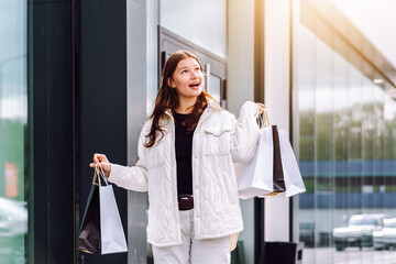 Joyful shopper celebrating discounts while carrying bags outside a modern store