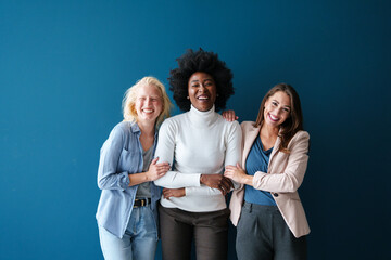 Three Multicultural Young Women Sharing Genuine Laughter Against Turquoise Background In Modern...