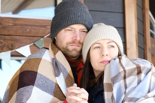 Couple relaxing on a patio wrapped on checkered blankets. Relaxed beautiful woman with a handsome man sitting on wooden cottage terrace. Winter resort. Happy loving couple enjoying leisure, embracing