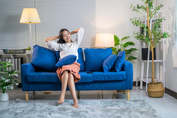 Obraz premium Asian woman stretching on blue sofa in modern living room enjoying leisure time at home