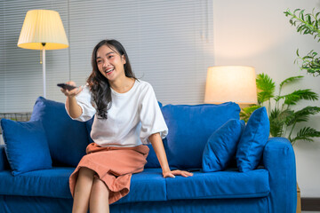 Young woman changing channels while laughing and watching television on blue couch