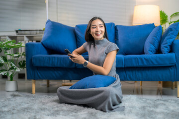 Obraz premium Happy asian woman using mobile phone while sitting on floor in living room