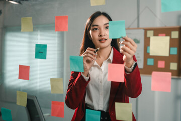 Businesswoman attaching sticky notes on glass wall and planning project schedule using sticky notes...