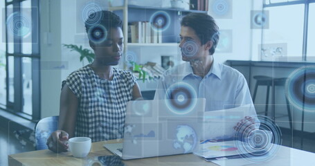 Collaborating colleagues analyzing holographic data overlays at office desk, with laptop and charts